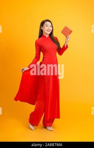 Jeune femme vietnamienne en robe traditionnelle ao dai, hand holding gift, célébrant le Nouvel An lunaire ou fête du printemps, un corps entier debout sur bac jaune Banque D'Images