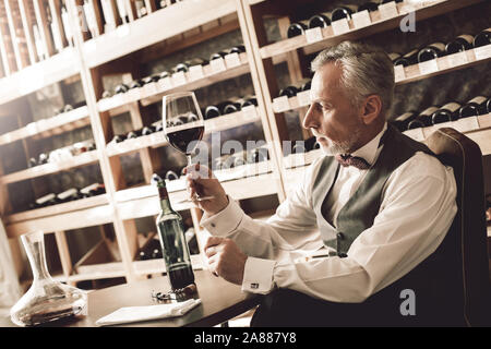 Sommelier Concept. Senior contrôle de sédiments dans le verre de vin rouge concerné Banque D'Images