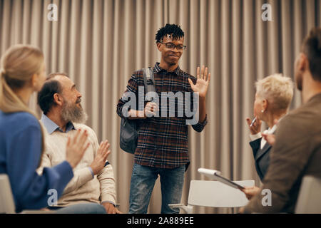 Jeune homme africain en lunettes et en agitant sa main permanent accueil il d'autres personnes dans la classe Banque D'Images