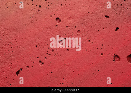 La texture d'un mur peint la plaque de ciment. fond de couleur rouge. mur avec bosses et petits trous. Banque D'Images
