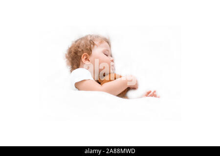 Petit bébé enfant dort sur un couvre-lit propre serrant un ours en peluche. Caucasien enfant fille garçon assis rêves sur grand lit, fond blanc. Cheveux bouclés, cl Banque D'Images