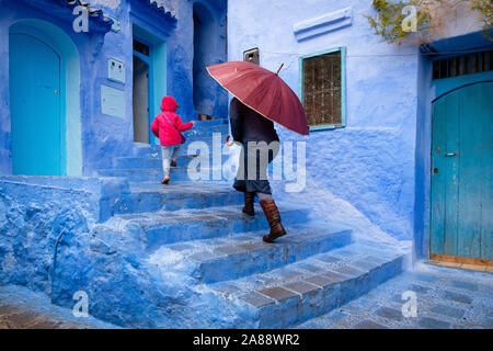 Maroc : Chefchaouen, la ville bleue. Femme et sa fille avec un parapluie dans une ruelle de la médina Banque D'Images