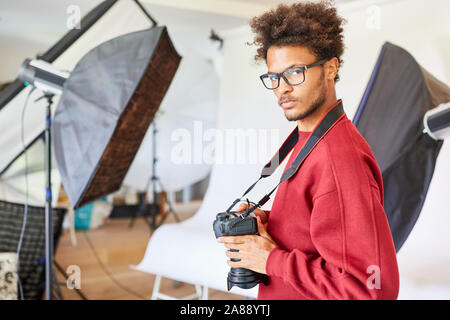 Jeune homme comme photographe pigiste avec appareil photo dans son studio photo Banque D'Images