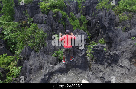 Homme avec chemise rouge grimper et randonnées dans la forêt de Rock (Hutan Batu) dans Rammang Rammang - Sud de Sulawesi - Indonésie Banque D'Images