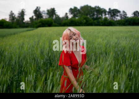 Femme aux cheveux roses portant une robe rouge dans le champ de blé Banque D'Images