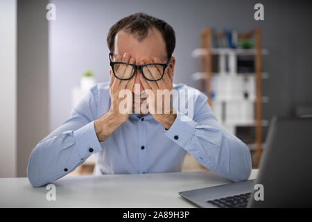 La main de l'homme sur le visage avec des lunettes In Office Banque D'Images