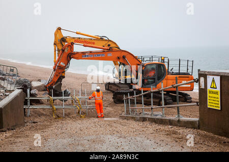 Des ouvriers avec des machines lourdes réparer le mur de protection contre les inondations à Torcross, Devon. Banque D'Images