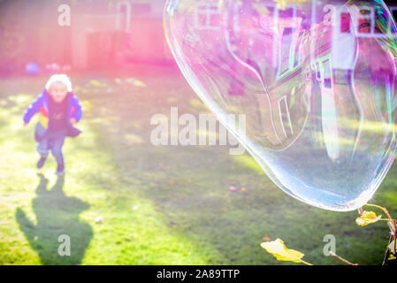 Enfant jouant à l'extérieur dans un jardin pendant la journée avec des bulles qu'il est heureux et en cours d'exécution Banque D'Images