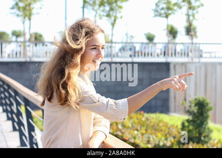 Beautiful teenager girl points avec un doigt quelque part. Happy girl élégante sur une journée ensoleillée Banque D'Images