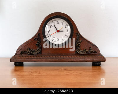 À l'ancienne, à l'horloge de bureau décorative. Vieux réveil contre un mur blanc debout sur le comptoir d'un bureau en bois. Banque D'Images