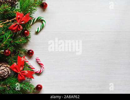 Composition de Noël, branches de sapin avec les cônes avec arcs rouges, des jouets et des bonbons sur un fond clair Banque D'Images