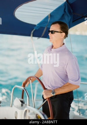 La classe moyenne d'un homme à la barre d'un voilier yacht charter de la côte de l'île de Tortola, Îles Vierges Britanniques Banque D'Images