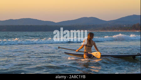 Une fille qui marche dans l'océan avec un stand up paddle board Banque D'Images