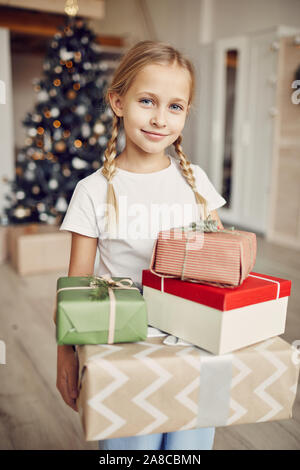 Portrait of little girl holding tas de cadeaux de Noël et à la caméra à tout en se tenant dans la chambre à la maison avec l'arbre de Noël Banque D'Images