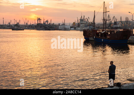 Varna, Bulgarie - 16 juillet 2014 : pêcheur se dresse sur un brise-lames dans le port de Varna au coucher du soleil Banque D'Images