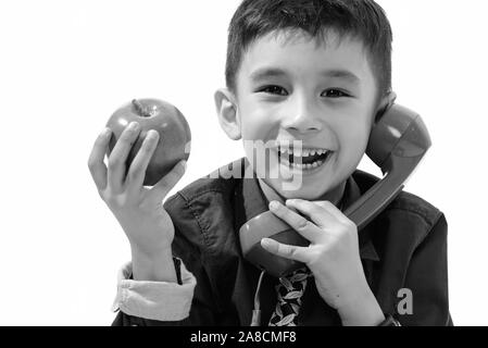 Studio shot of cute happy boy smiling and holding green apple tout en parlant sur l'ancien téléphone Banque D'Images