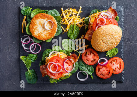 La Turquie fait maison sur les pains hamburger avec fromage, râpé en croustillant de lard grillé, tomates, épinards, l'oignon rouge sur une plaque en ardoise noire, Banque D'Images