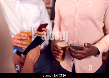 Groupe d'amis tous les téléphones mobiles de contrôle tout en répondant pour verre au bar Banque D'Images