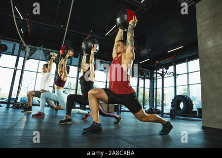 Un groupe d'athlètes musculaire faisant de l'exercice dans la salle de sport. La gymnastique, la formation, l'entraînement de fitness de flexibilité. Vie active et en santé, de la jeunesse, le culturisme. Mouvements brusques et des étirements en formation avec le ballon. Banque D'Images