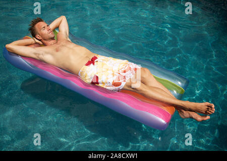 Young Caucasian man relaxing on un radeau flottant dans une superbe piscine Banque D'Images