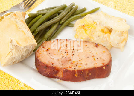 Côtelette de porc désossé fumé maison de vacances repas servi avec des haricots verts et gratin de pommes de terre gratinées au four et un rouleau de baguette. Tourné en lumière naturelle. Banque D'Images