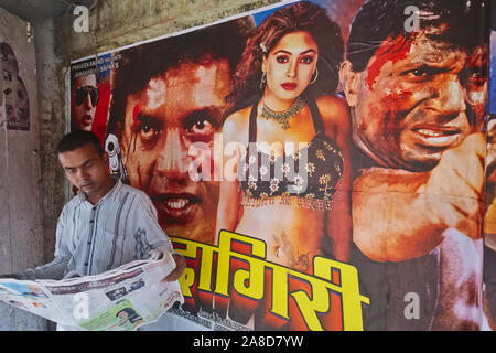 Un homme lit un journal devant une classe de travail bon marché l'industrie du cinéma dans la région de Grant Road de Mumbai, en Inde, le cinéma spécialisé dans les films hindi âgés Banque D'Images