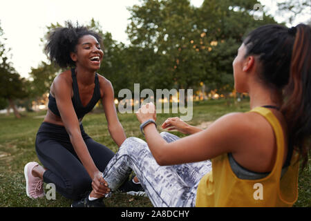 Young female friends laughing diversifiée faisant ab craque sur l'herbe verte dans le parc - les amis rient ensemble tout en faisant de l'exercice à l'extérieur Banque D'Images