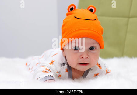 Le charmant bébé dans un chapeau orange se trouve sur une fourrure blanche sur l'estomac Banque D'Images