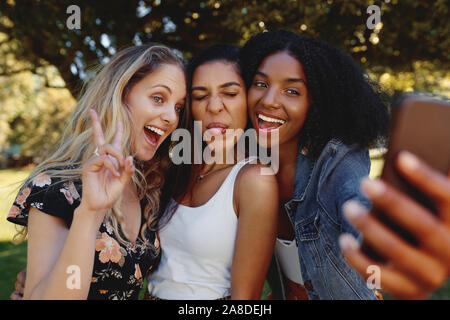 Portrait of a smiling young heureux diverses belles femmes proches amis s'amusant et en prenant sur selfies téléphone mobile dans le parc Banque D'Images