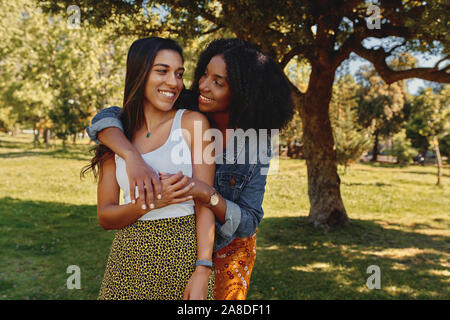 Portrait of a smiling happy young woman hugging diversifié ses amis et s'amuser dans le parc Banque D'Images