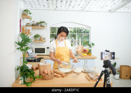 Jolie jeune femme d'origine asiatique food blogger travaille sur une nouvelle vidéo et d'expliquer comment cuisiner un plat Banque D'Images