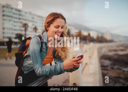 Close-up of a happy blonde jeune femme avec son sac à dos à l'aide du smartphone sur city street Banque D'Images