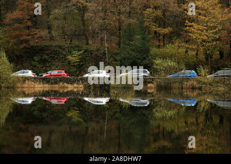 Voitures en stationnement reflète dans Yew Tree Tarn dans le Lake District, UK. Banque D'Images