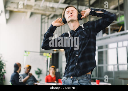 Happy young Caucasian woman in casual wear with earphones listening music et avoir briser dans Office. Son travail de l'équipe couronnée et discuter Banque D'Images