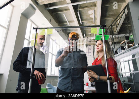 Multiethnical dans trois affaires d'examen et de planification de concept, travaillant ensemble en bureau loft avec paroi en verre. Avant de verre Banque D'Images