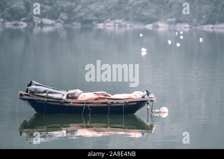 Un petit bateau à rames en bois laissé à flot dans les eaux vert émeraude près de Village de Cat Ba dans la baie d'Ha Long, au nord Vietname Banque D'Images