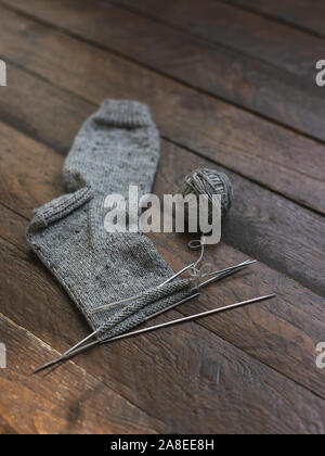 Chaussettes tricotées à la main avec des aiguilles et du fil gris sur fond de bois sombre ball. Concept pour la main et hugge slow life. Banque D'Images