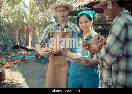 Un agriculteur familial debout à côté d'élevage de poulets, la fille holding a tablet et pointe le doigt pour expliquer son père et son frère pour l'agriculture wit Banque D'Images