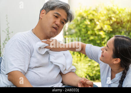 Et d'âge moyen des hommes obèses sont paralysés, la bouche de travers, plissés, une faiblesse des mains et dans le fauteuil roulant et il y a une femme à l'aide d'une serviette sur les f Banque D'Images