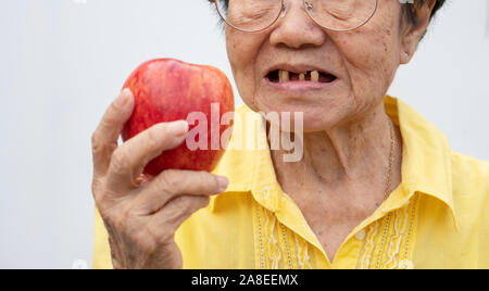 Une vieille femme porte des lunettes et sans dents en essayant de manger des pommes rouges. Concept de problèmes de santé dentaire, les patients âgés et les soins médicaux conc Banque D'Images