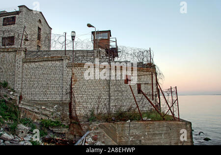 Mur de la prison fortifiée à côté de la mer. Des barbelés sur les murs. Tour de sécurité. Mer calme. Banque D'Images