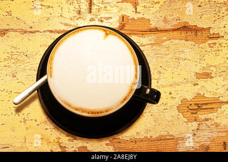 Tasse cappuccino café sur la vieille table en bois jaune pastel minable arrière-plan. Close up, mise à plat, vue du dessus. Banque D'Images