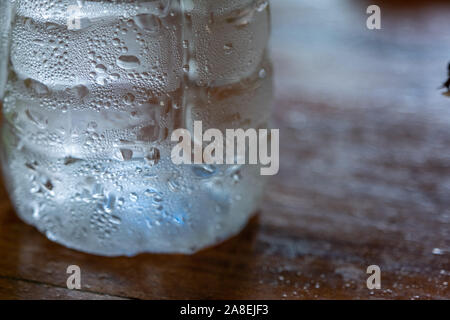 La goutte d'eau claire sur la bouteille d'eau fraîche sur la table en bois avec l'arrière-plan flou Banque D'Images