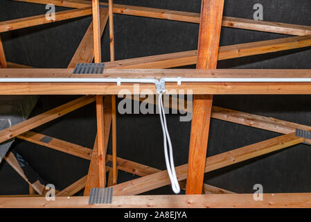 Les câbles d'éclairage en plastique dans les tuyaux de câblage dans une maison nouvellement construite montés sur des fermes de toit. Banque D'Images