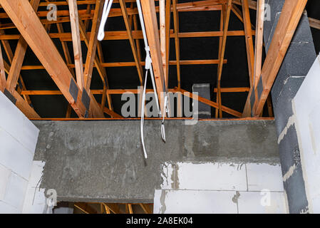 Les câbles d'éclairage en plastique dans les tuyaux de câblage dans une maison nouvellement construite montés sur des fermes de toit. Banque D'Images