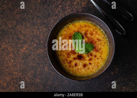 Bol ou tasse de crème brûlée à la menthe dessert bouchon et laisser sur table en pierre sombre arrière-plan, Vue de dessus, copiez l'espace. Dessert cuisine française Banque D'Images