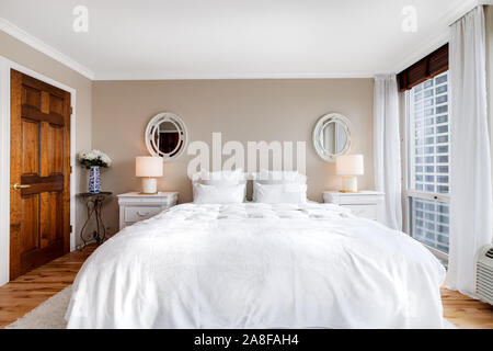 Une grande chambre principale situé au centre-ville de Chicago, avec un lit king size avec des draps blancs, des murs beiges, et de grandes portes de placard en bois. Banque D'Images