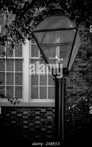 Une seule lampe à gaz de style ancien post allumée, près de white pans de fenêtres dans une maison en brique au crépuscule Banque D'Images