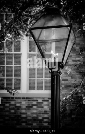 Une seule lampe à gaz de style ancien post allumée, près de white pans de fenêtres dans une maison en brique en noir et blanc Banque D'Images