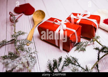 Deux boîtes de Noël rouge avec ruban blanc, d'une cuillère de bois, un cœur rouge et vert décoration sprouce sur une table en bois blanc. Banque D'Images